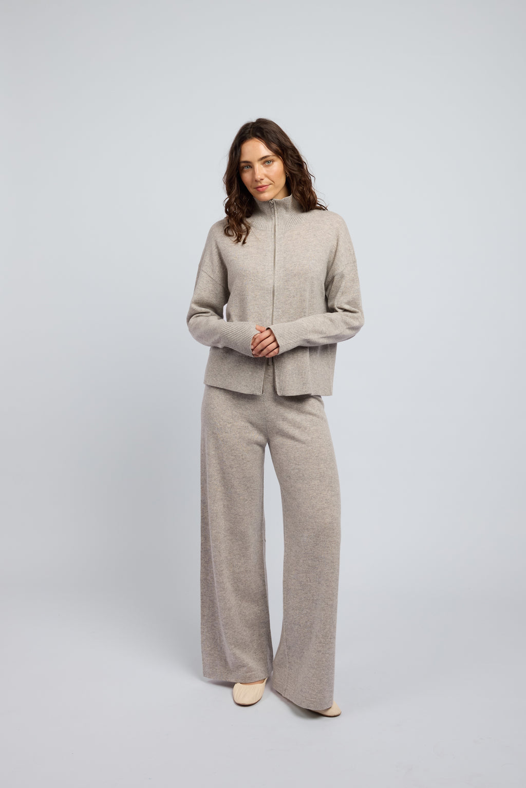 Woman wearing a cashmere set in light grey, matching pants and zip through jumper with a turtleneck collar