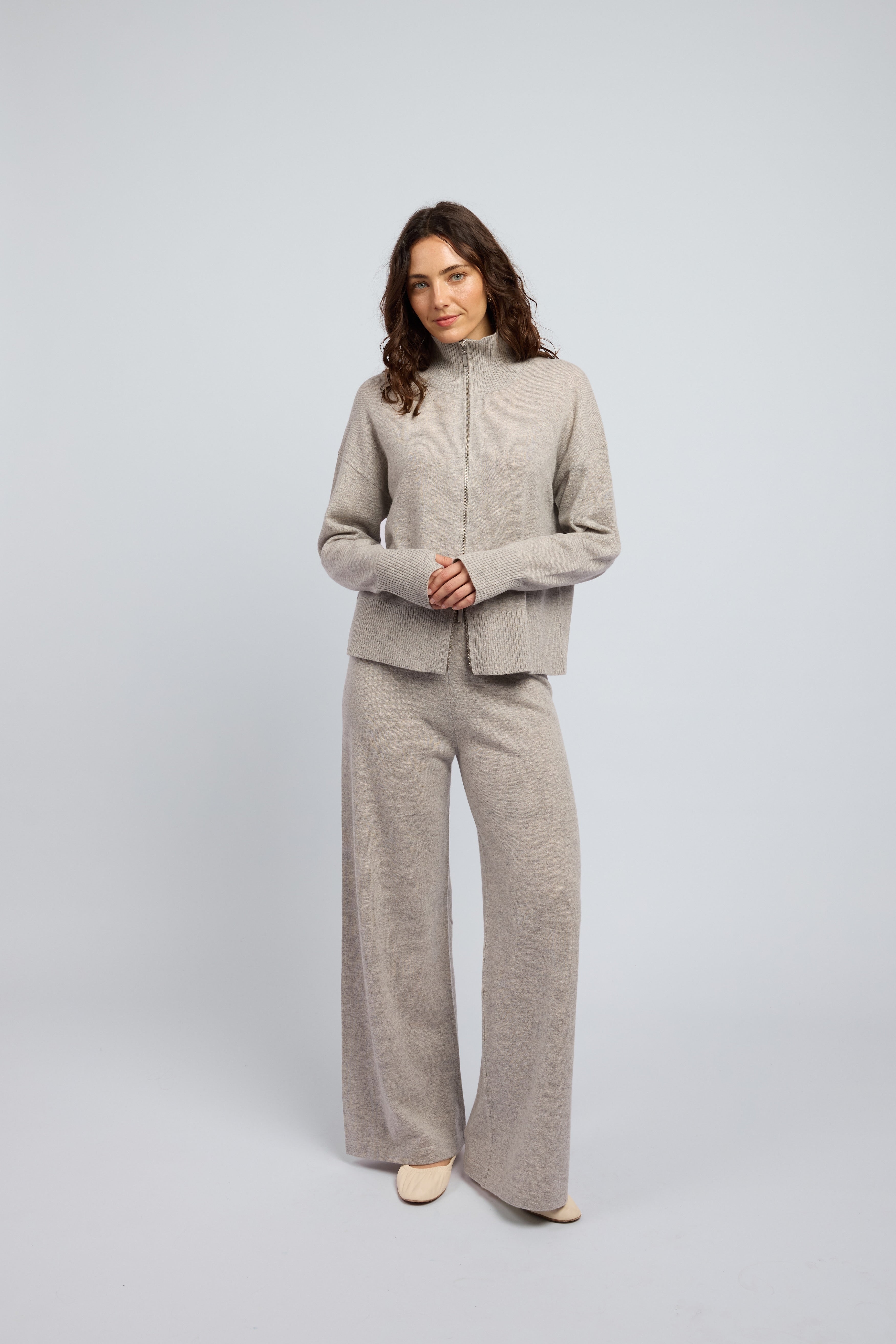 Woman wearing a cashmere set in light grey, matching pants and zip through jumper with a turtleneck collar