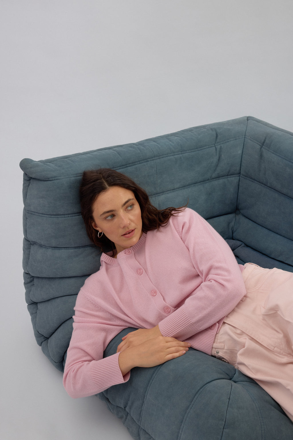 Woman wearing pink cashmere cardigan by Huntly Australia lounging on sofa