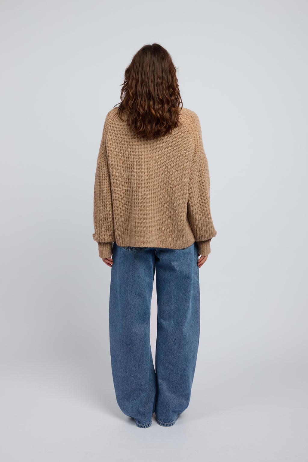 Woman wearing a beige and tan oversized cashmere sweater and blue jeans on a white background