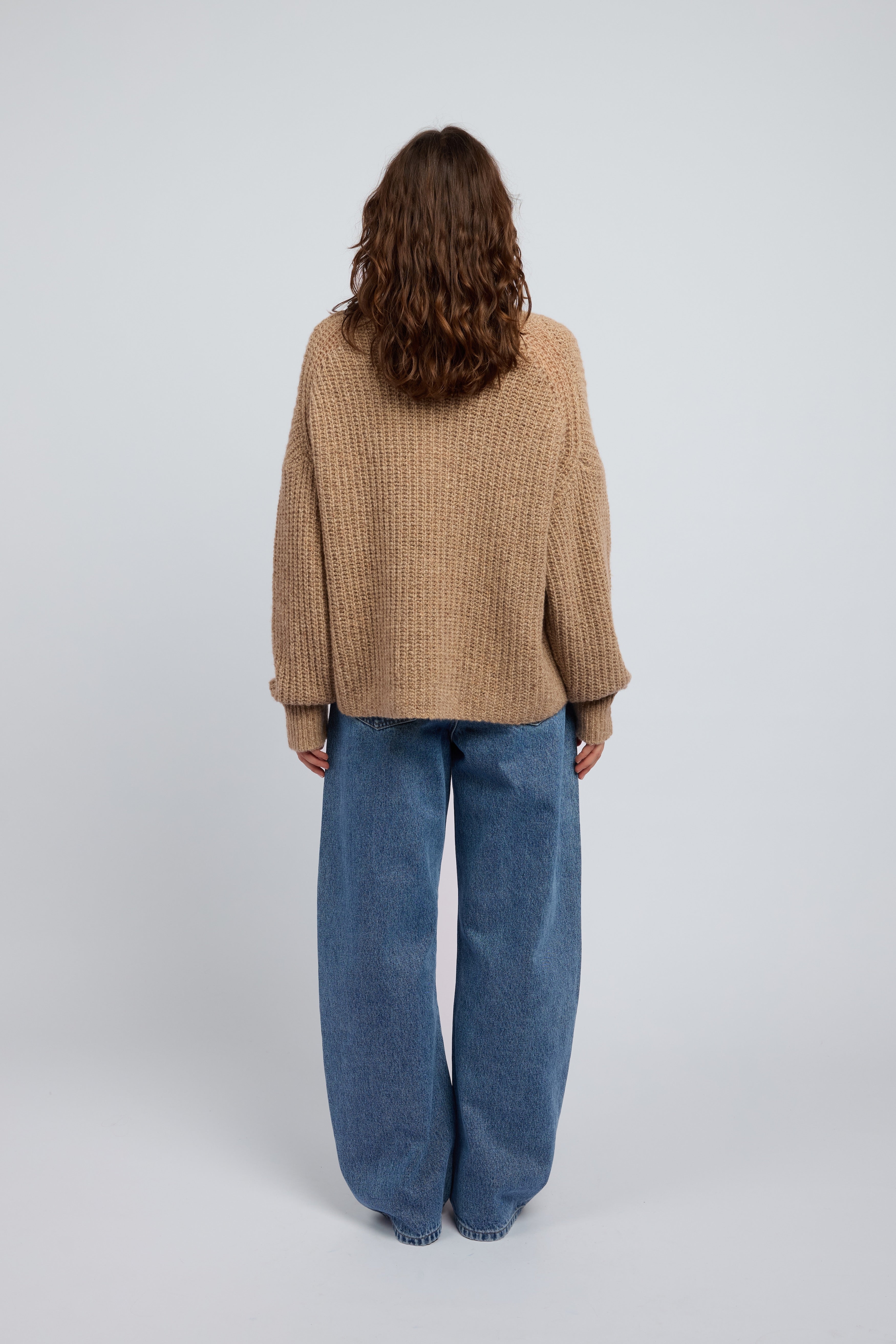 Woman wearing a beige and tan oversized cashmere sweater and blue jeans on a white background