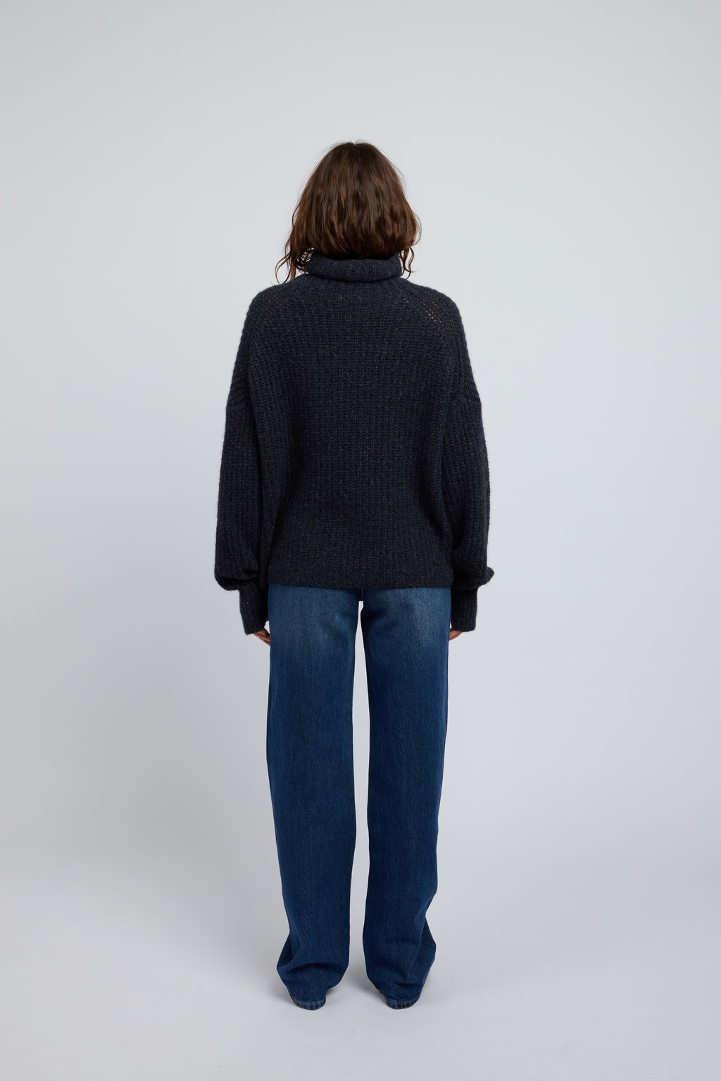Woman wearing a dark midnight navy cashmere turtleneck sweater and blue jeans on a white background with black point toe flats