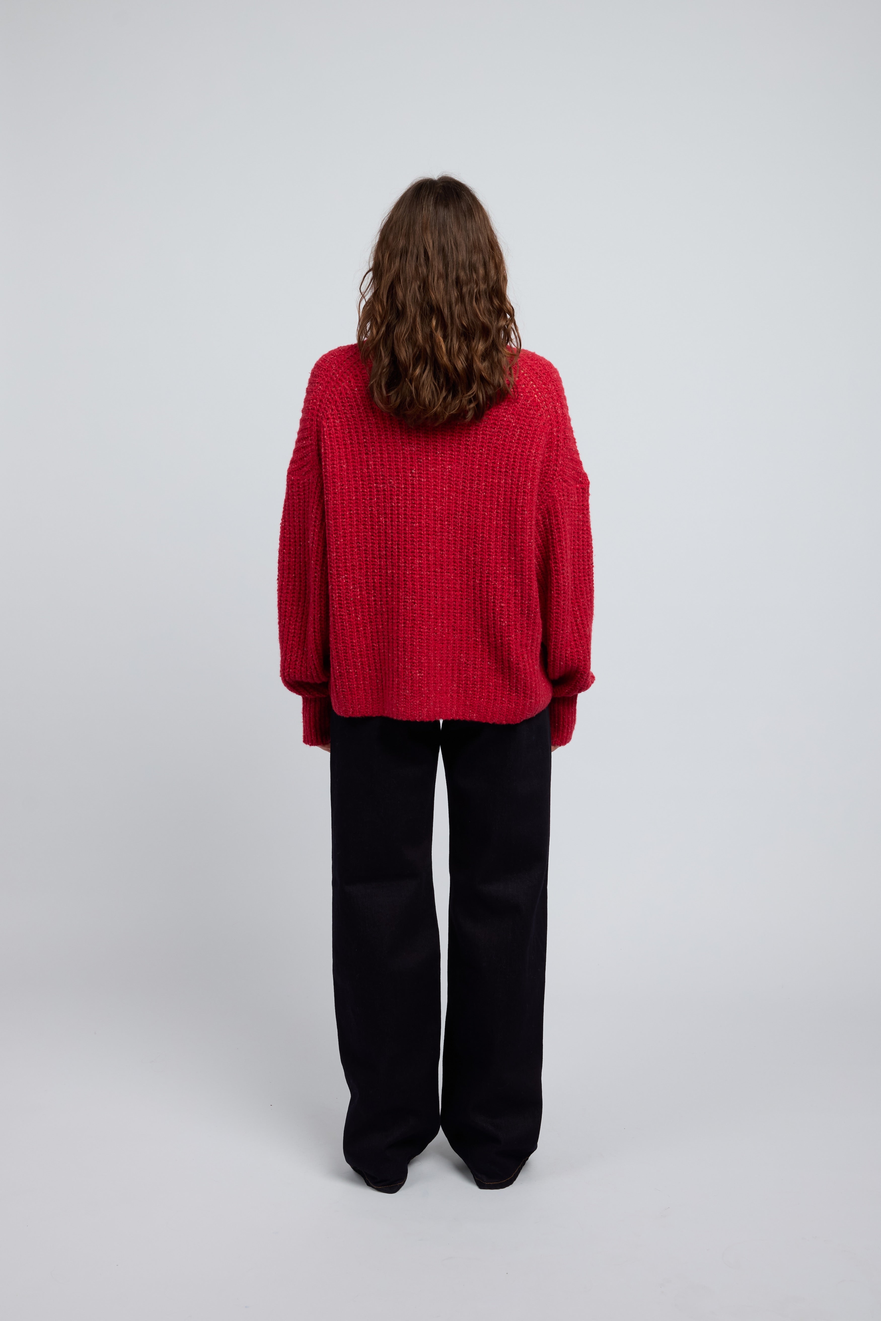 Woman wearing a poppy red cashmere turtleneck sweater and blue jeans on a white background
