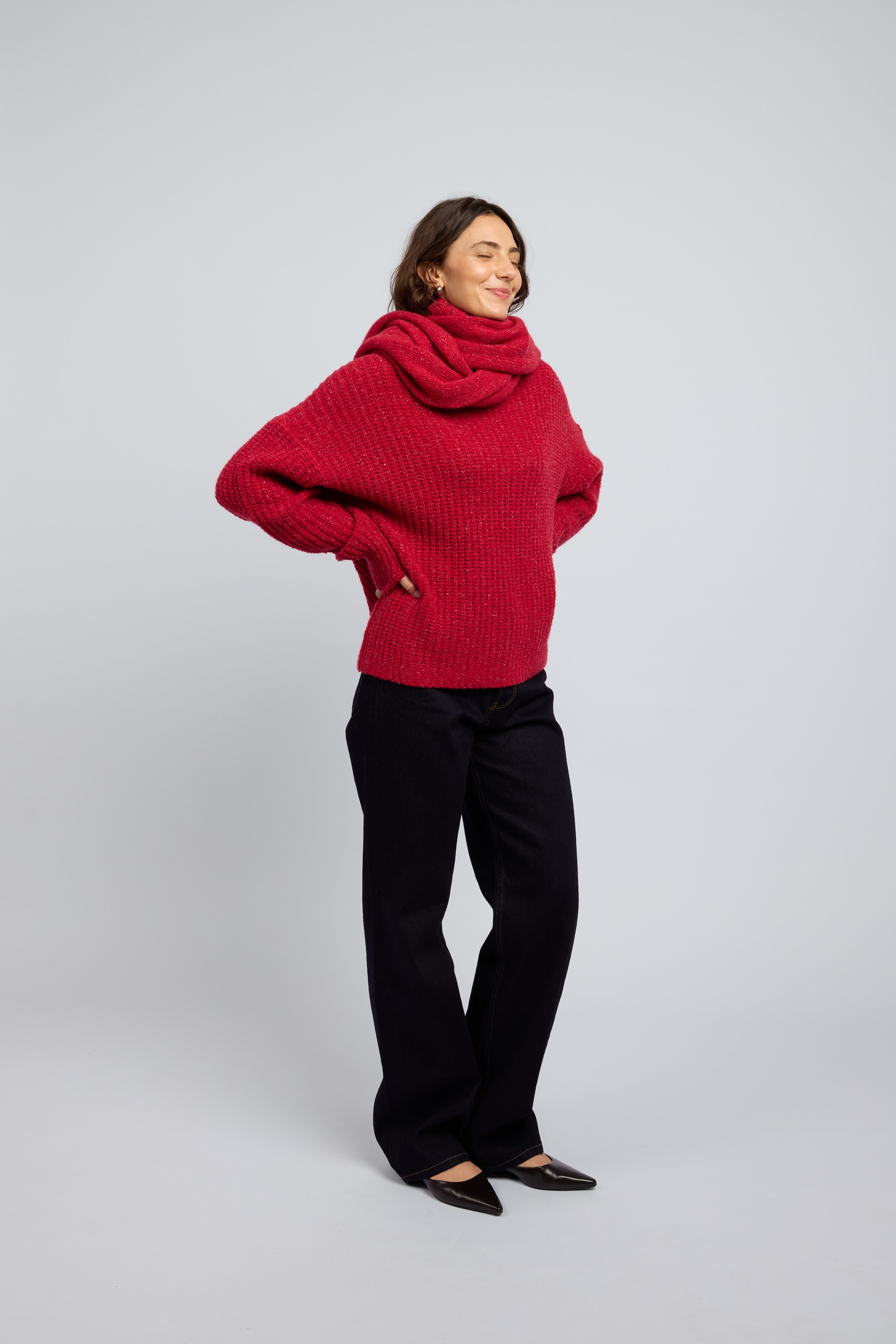 Woman wearing a poppy red cashmere turtleneck sweater and blue jeans and a matching chunky red scarf with black point toe flats