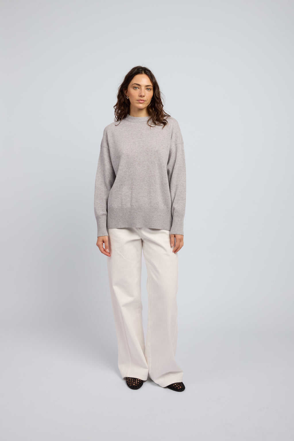 Woman wearing a light grey cashmere long sleeved sweater and white pants and black ballet flats