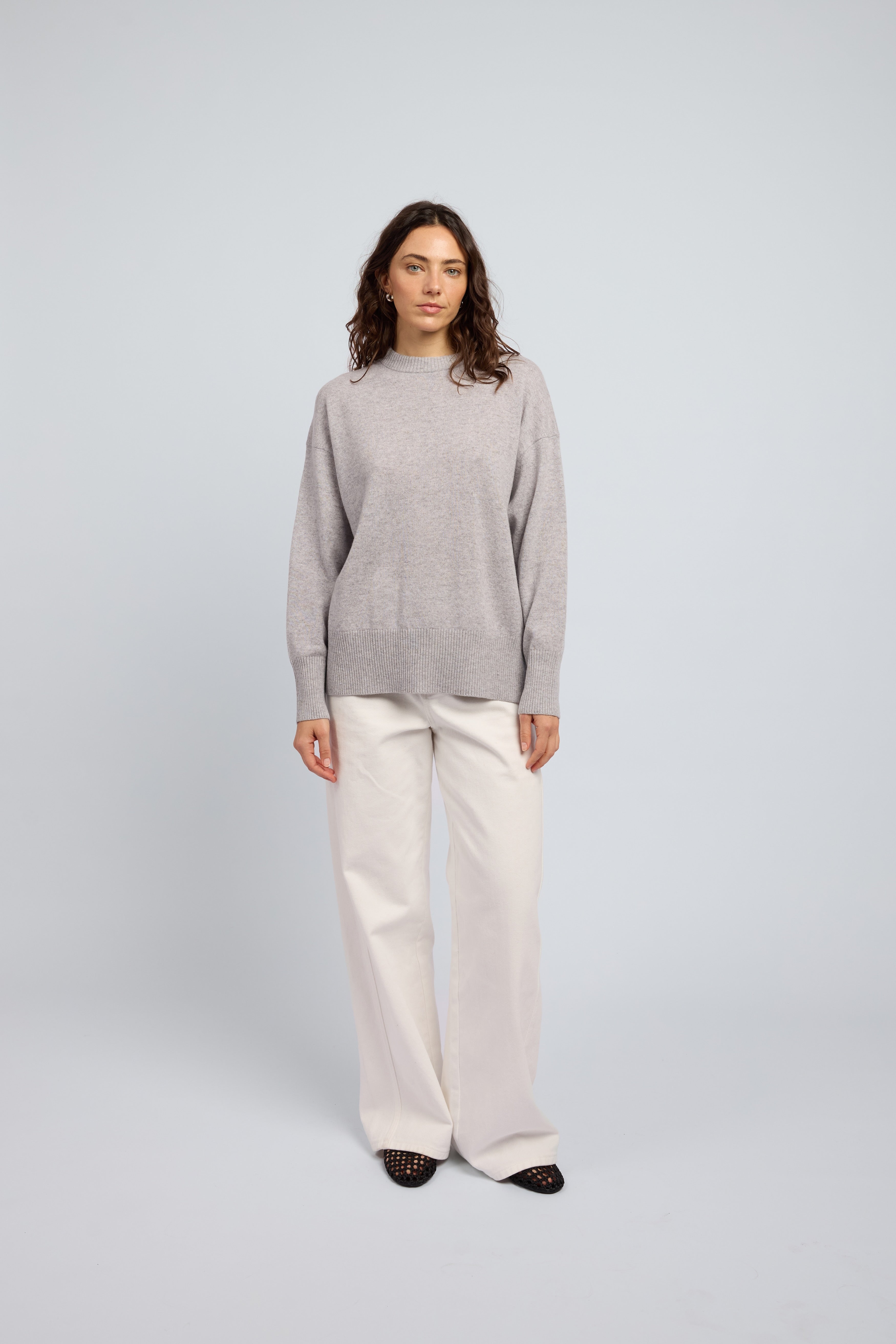 Woman wearing a light grey cashmere long sleeved sweater and white pants and black ballet flats