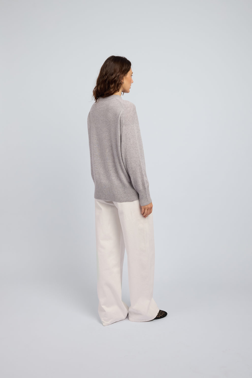 Woman wearing a light grey cashmere long sleeved sweater and white pants and black ballet flats