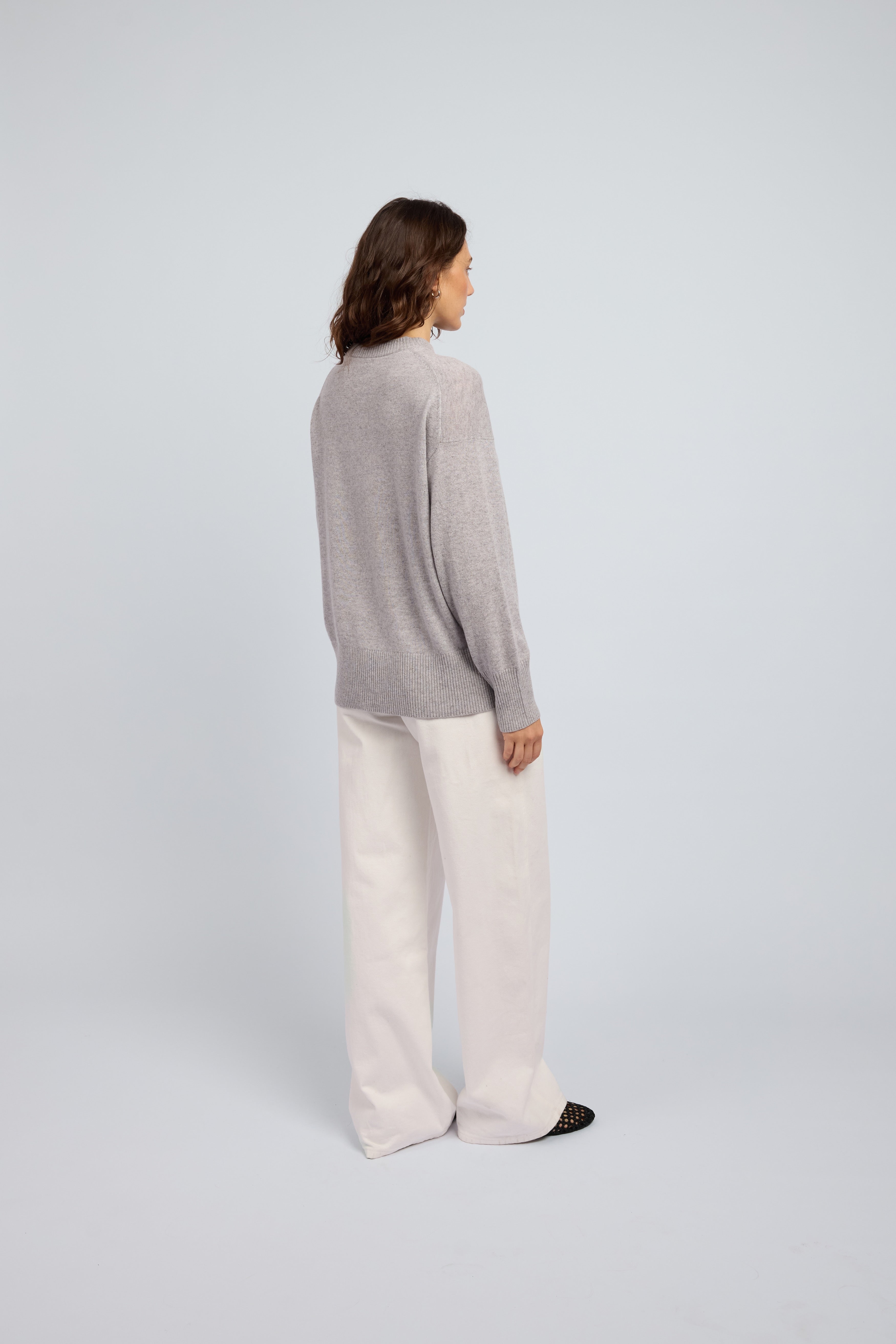 Woman wearing a light grey cashmere long sleeved sweater and white pants and black ballet flats